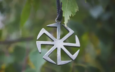 Metalowe koło symbolika, zawieszone na sznurku, na tle zielonych liści.