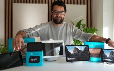 Mann präsentiert verschiedene Echo Show Generationen. Mehrere Geräte und Verpackungen sind auf dem Tisch zu sehen.