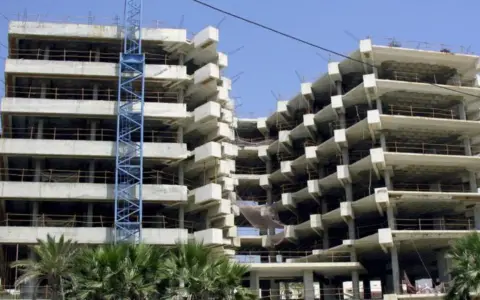 Edificio en construcción con grúa azul. La obra avanza lentamente, generando preocupación por sentencias de retraso en la entrega de vivienda de obra nueva.