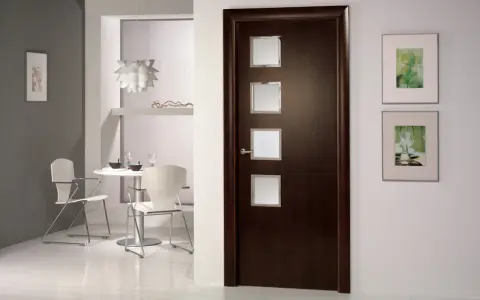 Puerta wengue con marcos de cristal. Paredes claras y un rincón de comedor moderno.