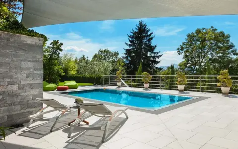 Moderne idee aiuole bordo piscina: piante in vaso e pouf colorati creano un'oasi rilassante.