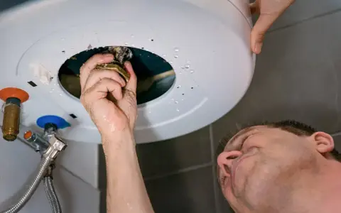 Main qui répare un chauffe-eau, une fuite d'eau s'échappe du cumulus qui fuit par le haut.