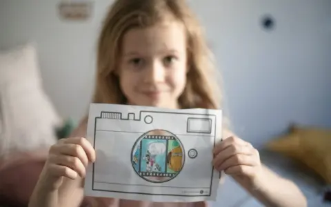 Uśmiechnięta dziewczynka pokazuje rysunek aparatu, przez który widać scenkę z pieskami. To świetna zabawa dla dziecka do lat 4 jak liczyć!