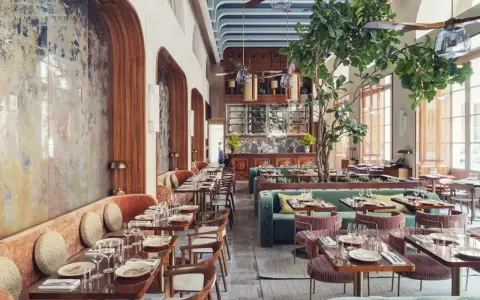 Intérieur d'un restaurant au style restauration architecture, avec banquettes velours, tables dressées et un arbre luxuriant au centre.