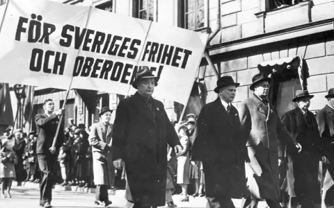 Män i hatt och rock marscherar med en banderoll: "För Sveriges frihet och oberoende!". En bild som speglar socialdemokraterna historia.