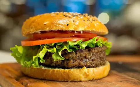 Apetyczny hamburger z sezamem, sałatą i pomidorem na desce.