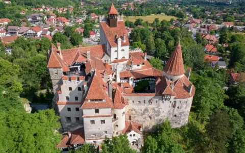 Dracula zamek, majestatyczna twierdza z czerwonymi dachami, otoczona zielenią i malowniczą wioską.