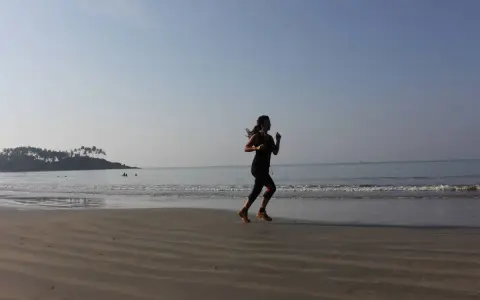 Mujer corriendo en la playa al amanecer, con el mar y una isla con palmeras al fondo.
