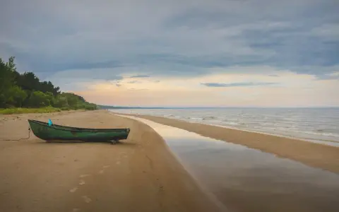 Zielona łódź na piaszczystej plaży Mierzei Wiślanej, idealne miejsce na camping. Woda odbija niebo, tworząc spokojny krajobraz.