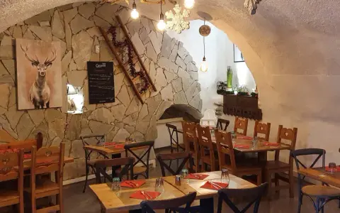 Ambiance chaleureuse dans un des restaurants de Briançon. Murs en pierre, tables en bois, tableau de menu et décoration hivernale.