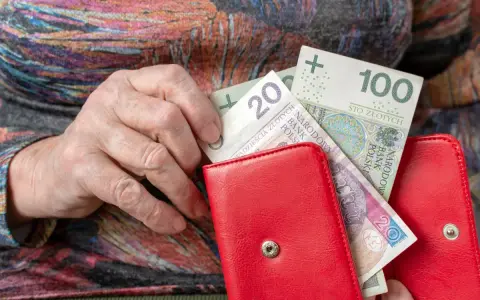 Dłoń starszej osoby wkłada pieniądze do czerwonego portfela. Może to być dodatek mieszkaniowy.