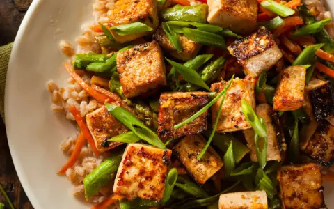 Chrupiące kostki tofu z warzywami i kaszą na talerzu.