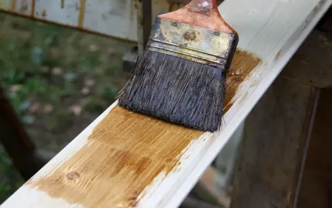 Pinceau appliquant une lasure sur une planche de bois clair, montrant la facilité de lasurer sans poncer pour une finition rapide et efficace.