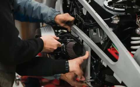 Mechanicy pracują nad motocyklem, być może rozwiązując problem zapchanego filtra paliwa powodującego szarpanie.
