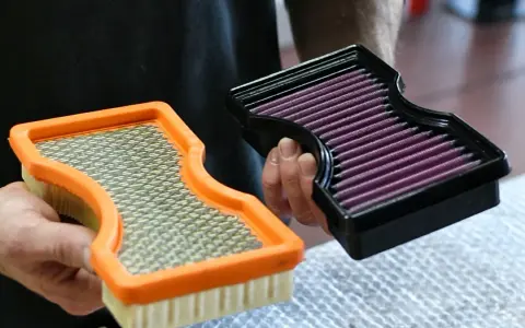 Hände halten zwei Luftfilter: einen orangen Standardfilter und einen schwarzen Sportluftfilter. Was bringt ein Sportluftfilter? Mehr Leistung!