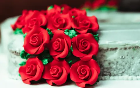 Un mazzo di rose rosse in pasta di zucchero adorna una torta.