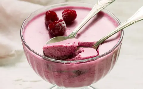 Himbeere-rotweincreme selbstgemacht in einer Glasschale, garniert mit frischen Himbeeren und zwei Löffeln.