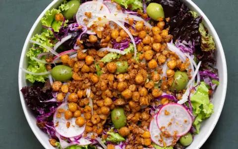 Ensalada colorida con garbanzos fritos crujientes, aceitunas verdes, lechugas variadas, rábano y cebolla morada.