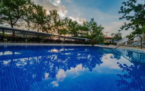 Błękitny basen z odbiciem drzew i chmur. Idealne miejsce na wakacje, zgodnie z **Senza Garden Holiday Club opinie**.