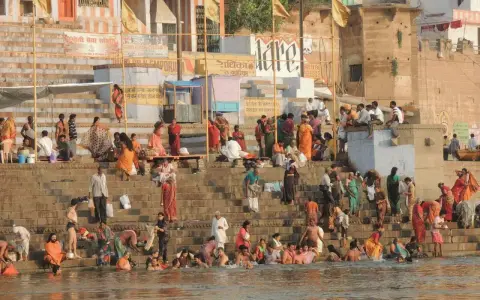 Tłum ludzi w barwnych strojach kąpie się i odpoczywa na schodach nad rzeką Ganges.