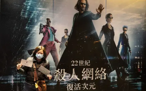 Donna con mascherina mostra biglietti davanti al poster di Matrix, con Neo e Trinity in primo piano. La trama di Matrix è avvincente.