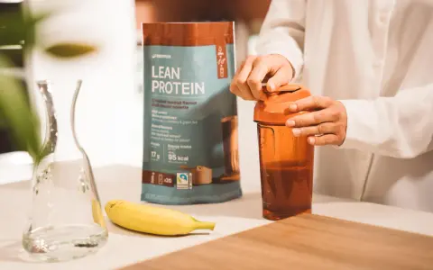 Eine Person bereitet einen Proteinshake zu. Die Packung "Lean Protein" zeigt 17g Protein pro Portion. Die Frage "wie viel protein pulver auf 500 ml" wird durch die Zubereitung beantwortet.