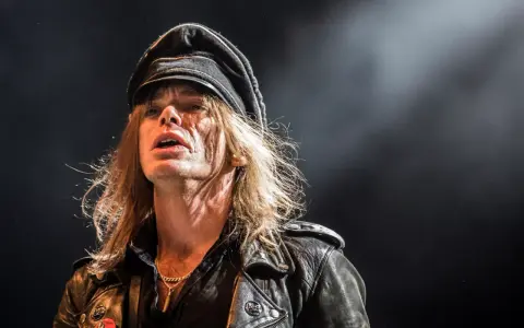 Nicke Andersson från Hellacopters, med sin karaktäristiska keps och läderjacka, fångad i ett intensivt ögonblick på scenen.