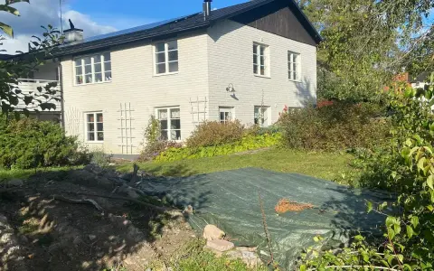 Vitt hus med mörk tak och trädgård. En presenning täcker en del av trädgården, kanske ett gömt hus skatt?