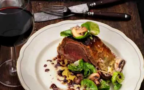 En saftig wellington biff serveras med svamp och grönsaker, ackompanjerad av ett glas rött vin.