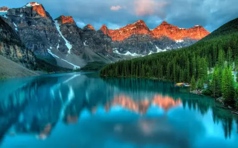 Turkusowe jezioro odbija ośnieżone szczyty gór o zachodzie słońca. W tle gęsty las iglasty. Park narodowy Banff zachwyca.