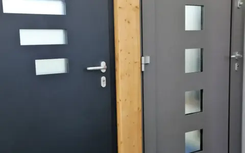 Dwie nowoczesne drzwi wejściowe, ciemnoszare i szare, z przeszkleniami. Ocieplenie drzwi wejściowych to klucz do komfortu.