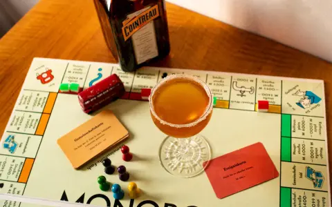 Ein Sidecar Cocktail steht auf einem Monopoly-Spielbrett neben einer Flasche Cointreau.