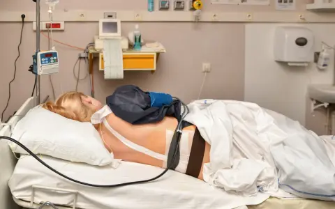 Pacjentka w łóżku szpitalnym z aparaturą medyczną. Widać cewnik z lekiem, co może być związane z pytaniem: epidural co to.