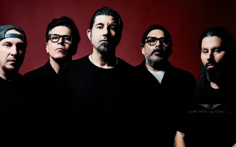 Pięciu mężczyzn, zespół Deftones Polska, pozuje do zdjęcia na ciemnoczerwonym tle.
