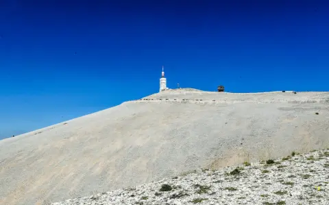 Le Mont Ventoux, sommet aride sous un ciel bleu intense, dominé par une tour de télécommunication.