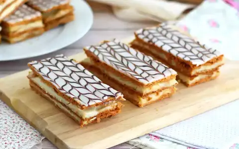Tre läckra millefeuille-bakelser med lager av smördeg och kräm, toppade med vit glasyr och chokladmönster.