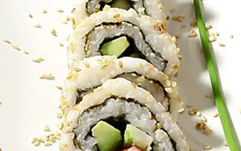 En närbild på en california roll med sesamfrön och en grön garnityr.