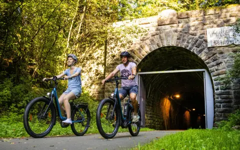 Ein Paar genießt eine entspannte Sauerland Fahrradtour, radelt auf E-Bikes am Eingang des Kuckelheimer Tunnels entlang.