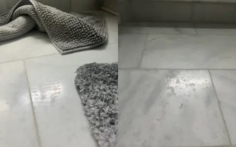 Grå badrumsmattor på marmorgolv. Vattenfläckar syns på golvet, vilket indikerar behov av marmor polering för att återställa glansen.