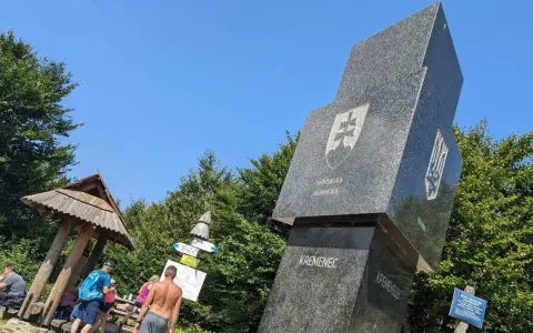 Trójstyk granic Bieszczady: monument z herbami Słowacji i Ukrainy, drewniana wiata i turyści.