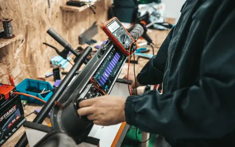 Naprawa i regeneracja akumulatorów hydraulicznych hulajnogi elektrycznej. Multimetr mierzy napięcie ogniw.