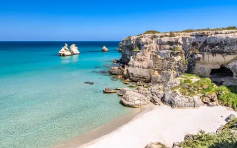Scogliere calcaree e mare cristallino a Torre dell'Orso centro, con faraglioni che emergono dall'acqua turchese.