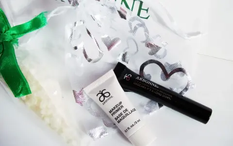 Arbonne opinie: zestaw kosmetyków z primerem i tuszem, w ozdobnym woreczku.