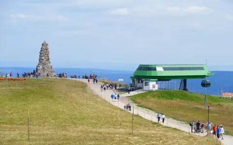 Feldberg: Steinkegel-Denkmal und Seilbahnstation mit Wanderern auf einem grasbewachsenen Hügel.