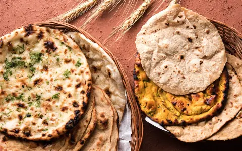 Dwa koszyki pełne pysznego chleba indyjskiego, w tym aromatyczny naan z kolendrą i klasyczny roti, ozdobione kłosami zboża.