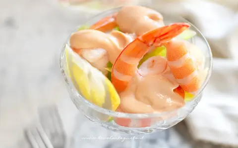 Un delizioso cocktail di gamberi servito in una coppa di cristallo, con una fetta di limone e una salsa rosa cremosa.