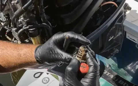 Mains gantées tenant un thermostat usagé, prêt pour le changement sur un moteur hors bord Yamaha.