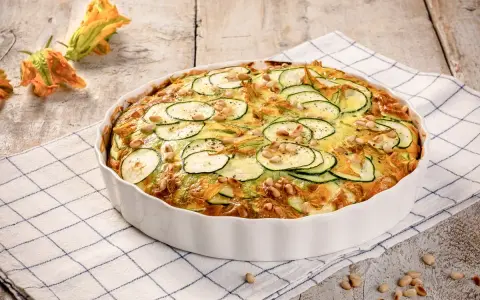 Frittata di zucchine al forno, guarnita con pinoli e fiori di zucca, pronta per essere gustata.