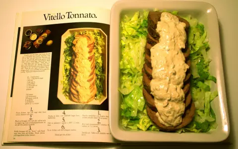 Vitello tonnato recept: skivad kalv med tonfisksås och sallad, bredvid en öppen kokbok med recept.