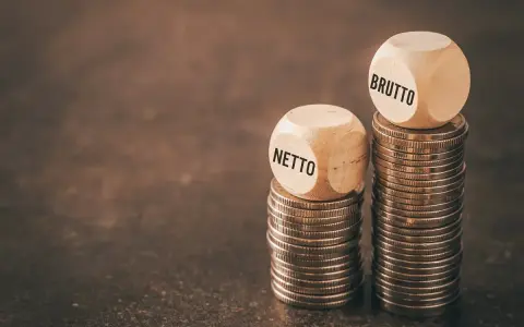 Dwie wieże monet, jedna z kostką "NETTO", druga z "BRUTTO". Symbolizuje to rozważania nad umową zlecenie i stawką godzinową.